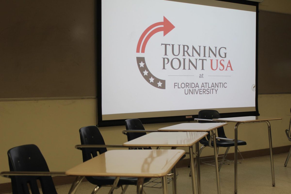 Classroom with empty desks facing a projection screen showing the Turning Point USA logo and “Florida Atlantic University” chapter name.