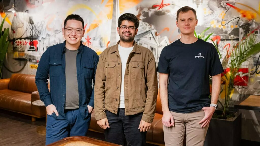 Founders of Perplexity AI — Johnny Ho, Aravind Srinivas, and Denis Yarats — standing together in front of a colorful mural in a modern office lounge.
