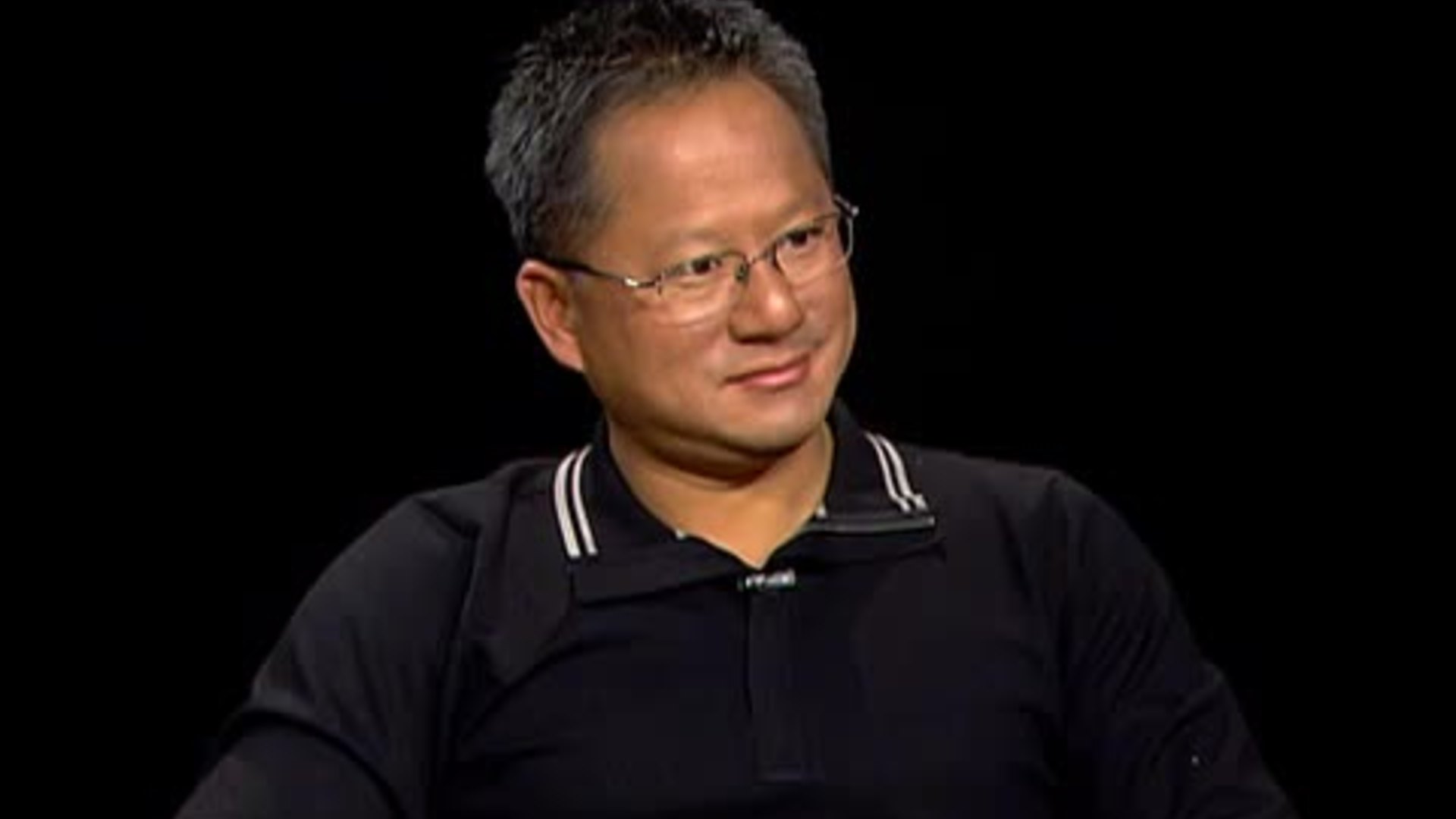 Jensen Huang in a 2006 interview setting, wearing glasses and a dark shirt, speaking calmly against a dark background.