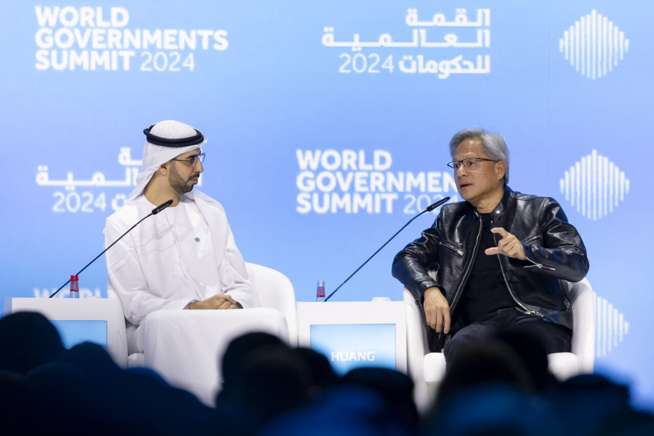Jensen Huang speaking on stage with a moderator at the World Government Summit 2024 in Dubai, discussing artificial intelligence and technology policy.