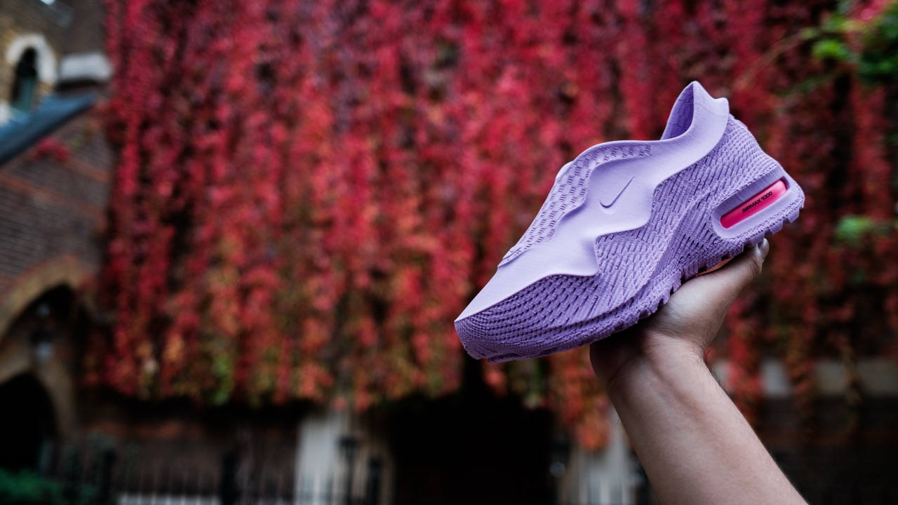 Nike Air Max 1000 in Lavender – Tumisang Bogwasi A hand holding a lavender Nike Air Max 1000 sneaker with a textured upper and visible pink Air unit, against a blurred red foliage background.
