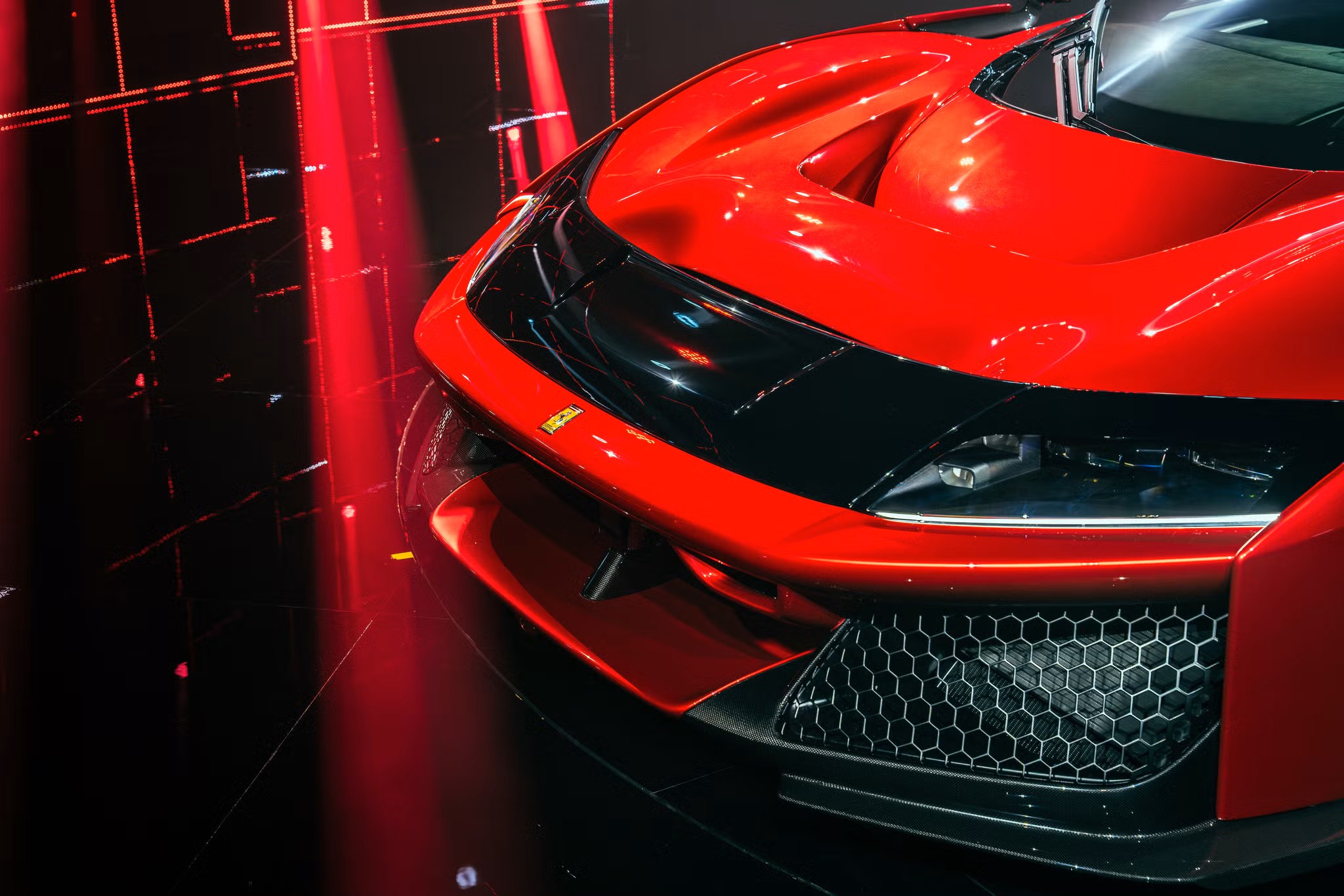 Ferrari F80 Front Detail Under Red Studio Lights – Tumisang Bogwasi Close-up of a red Ferrari F80 front end with sharp headlights and black grille, lit by red vertical lights in a dark studio setting.